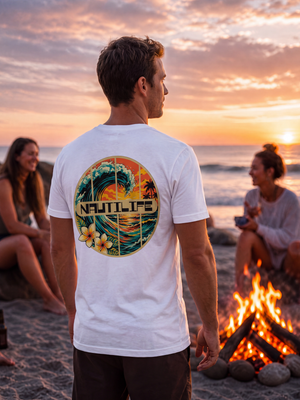A man standing on a beach at sunset wearing a white t-shirt with a large circular 'Nautilus' graphic on the back, with two women sitting nearby by a campfire.